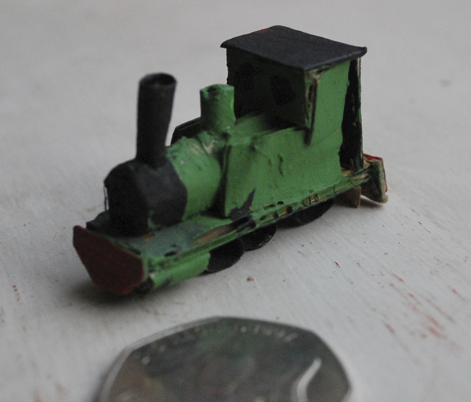 Tiny handmade green locomotive next to a coin