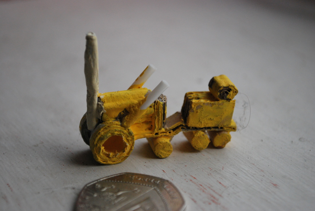 Tiny handmade yellow tractor next to a coin