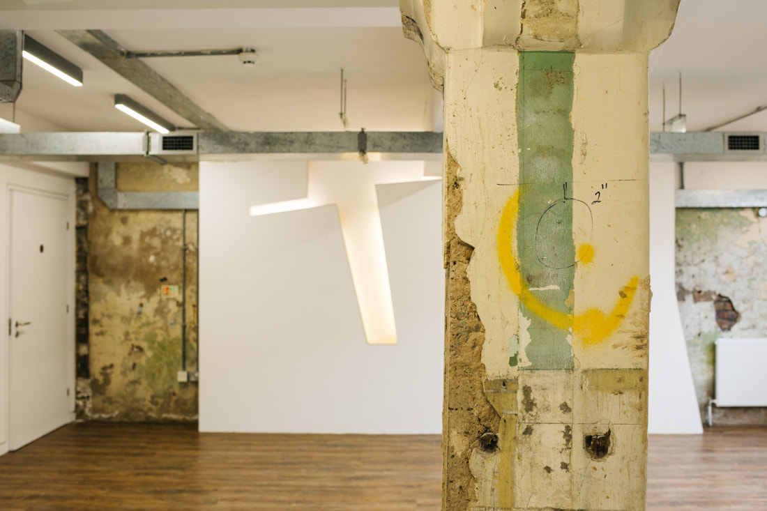 Raw structural column standing in foreground against a new illuminated white wall feature