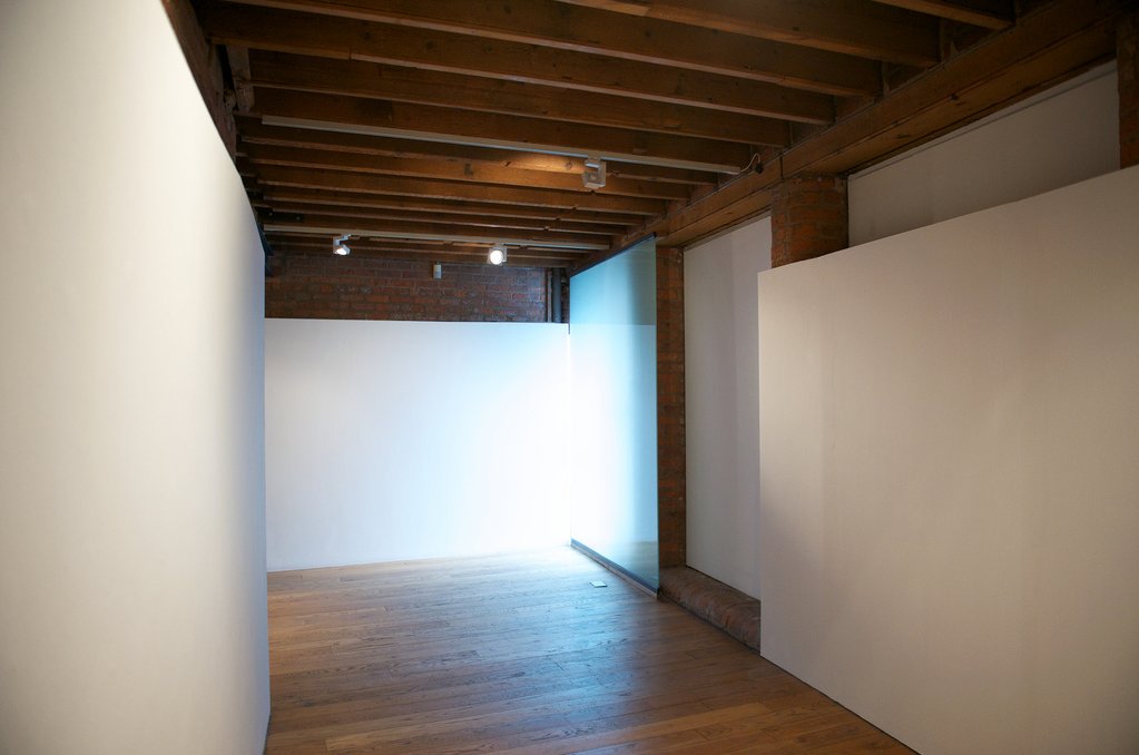Gallery corridor — white walls, translucent glass panel, brick and timber ceiling