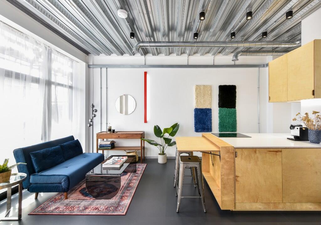 Apartment living space — blue sofa, birch ply kitchen, industrial ceiling