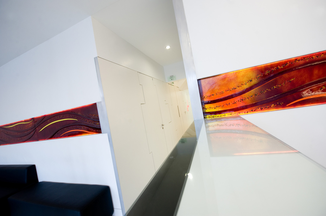 Waiting area — fused glass art panels, dark sofa, white walls