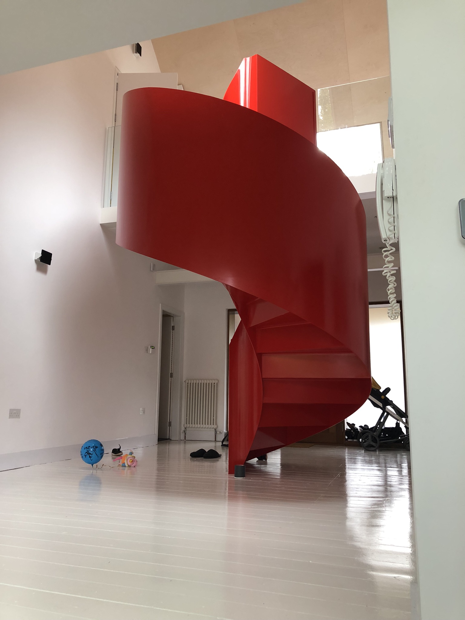 A brilliant red, sculptural steel helical stair in a bright white hallway