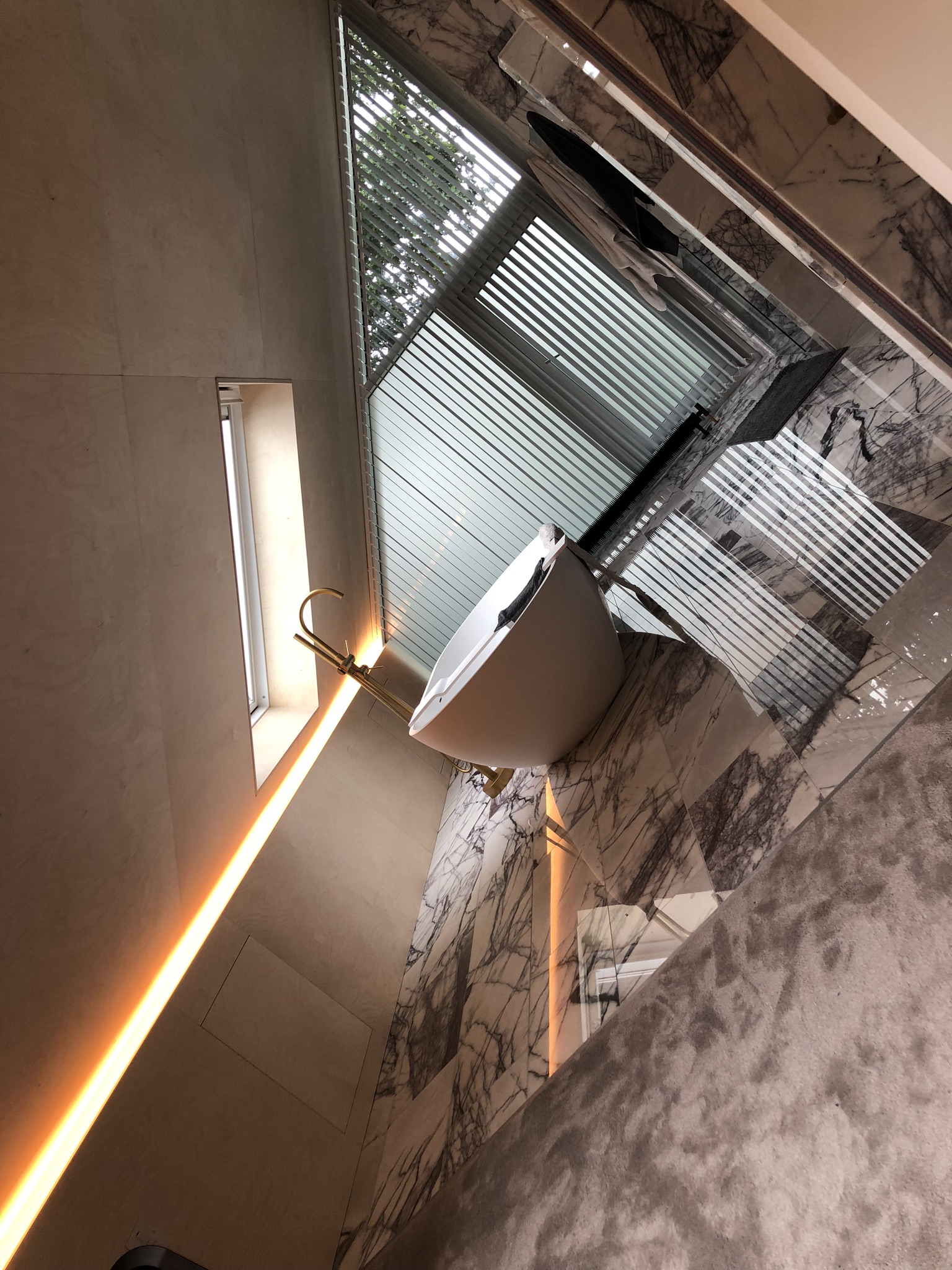 Freestanding white bath on an Italian marble floor beneath an angled window