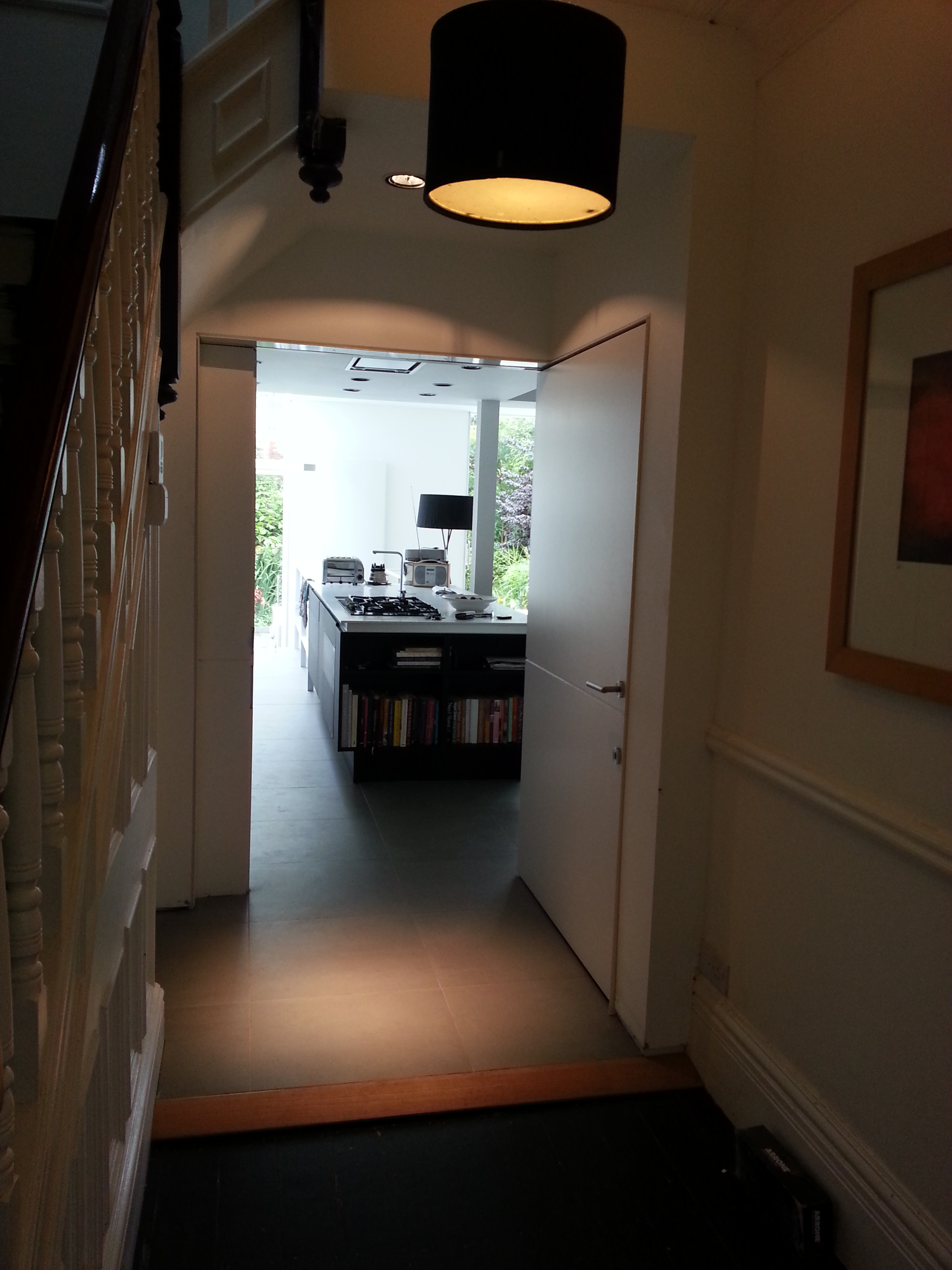 Bright, wide view of a minimalist black kitchen looking out through a large window to a green garden