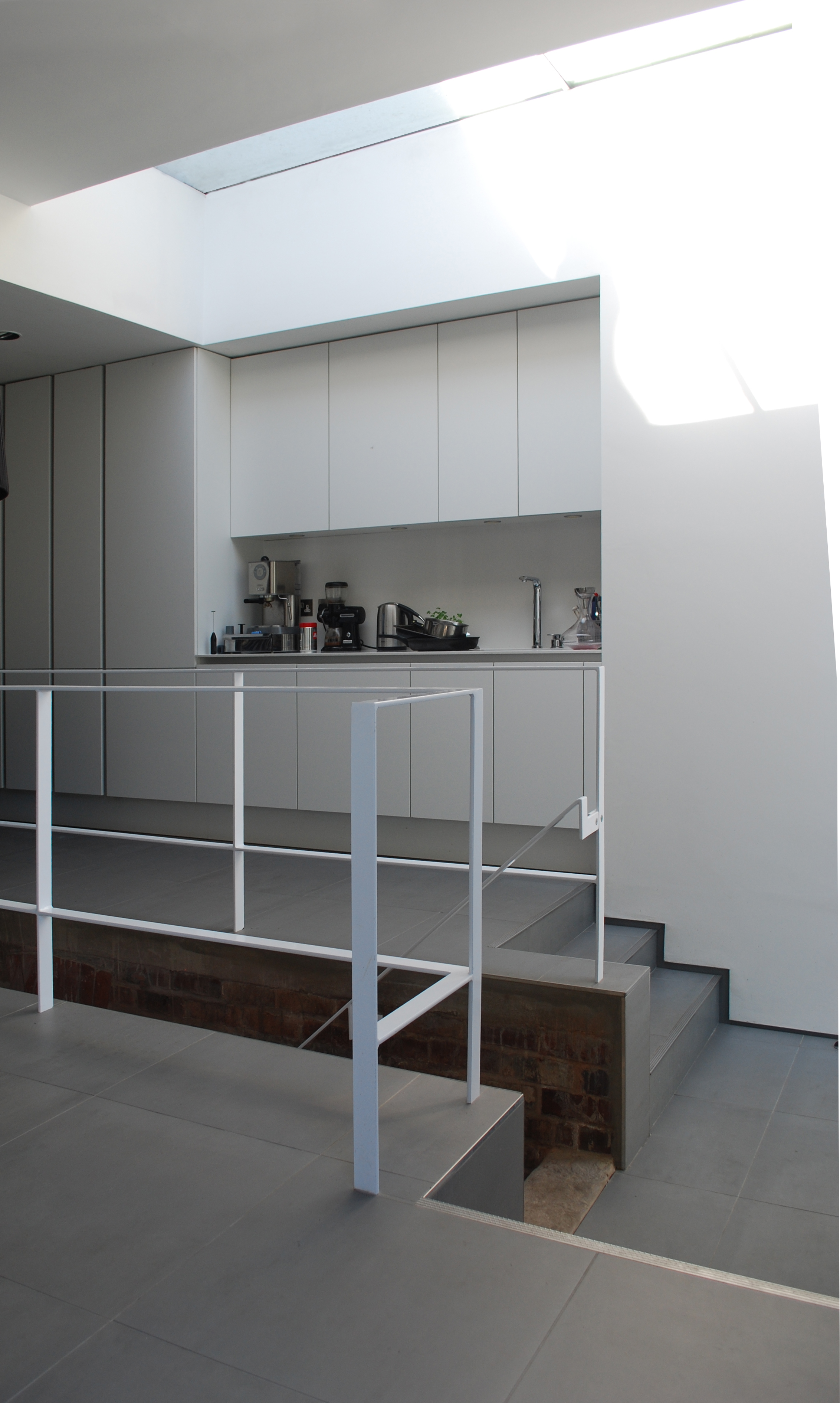 Minimalist white steel handrail and grey tiled steps showing a drop in floor level with exposed brick beneath