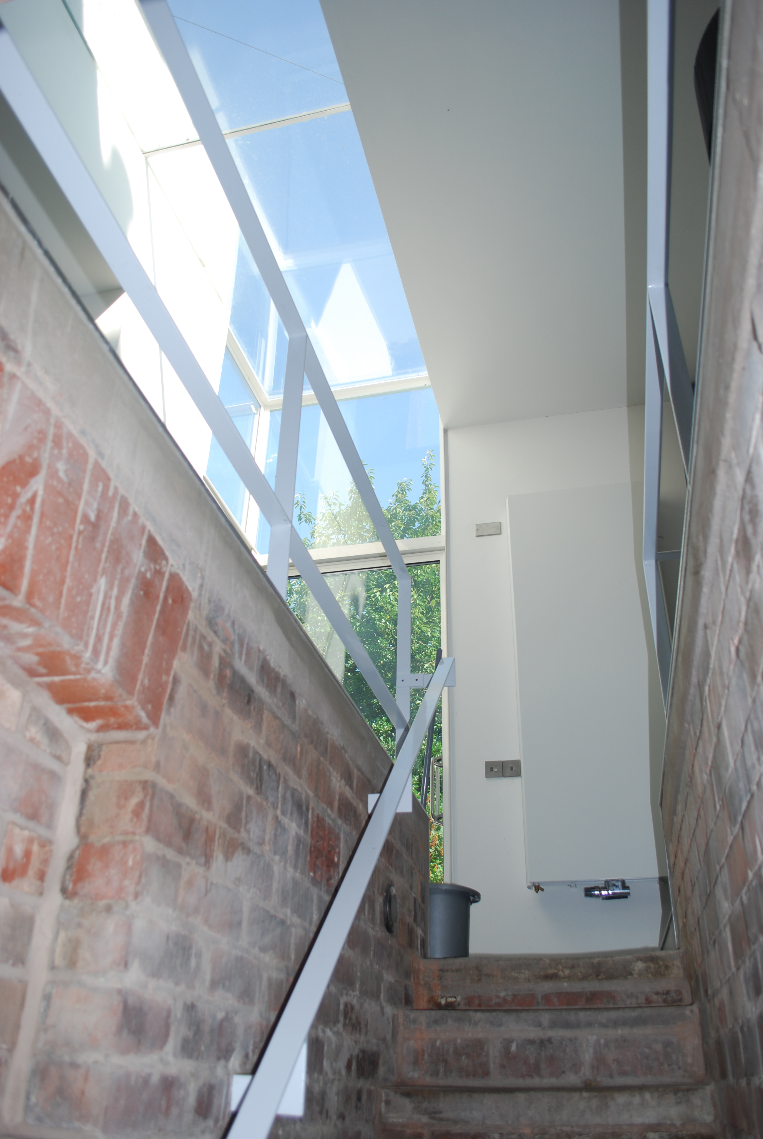 Looking up a stairwell beside an exposed, rough brick wall towards a bright skylight