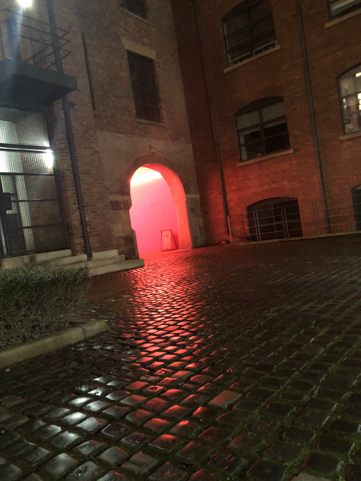 Red-lit entrance tunnel at night, light spilling onto cobblestones