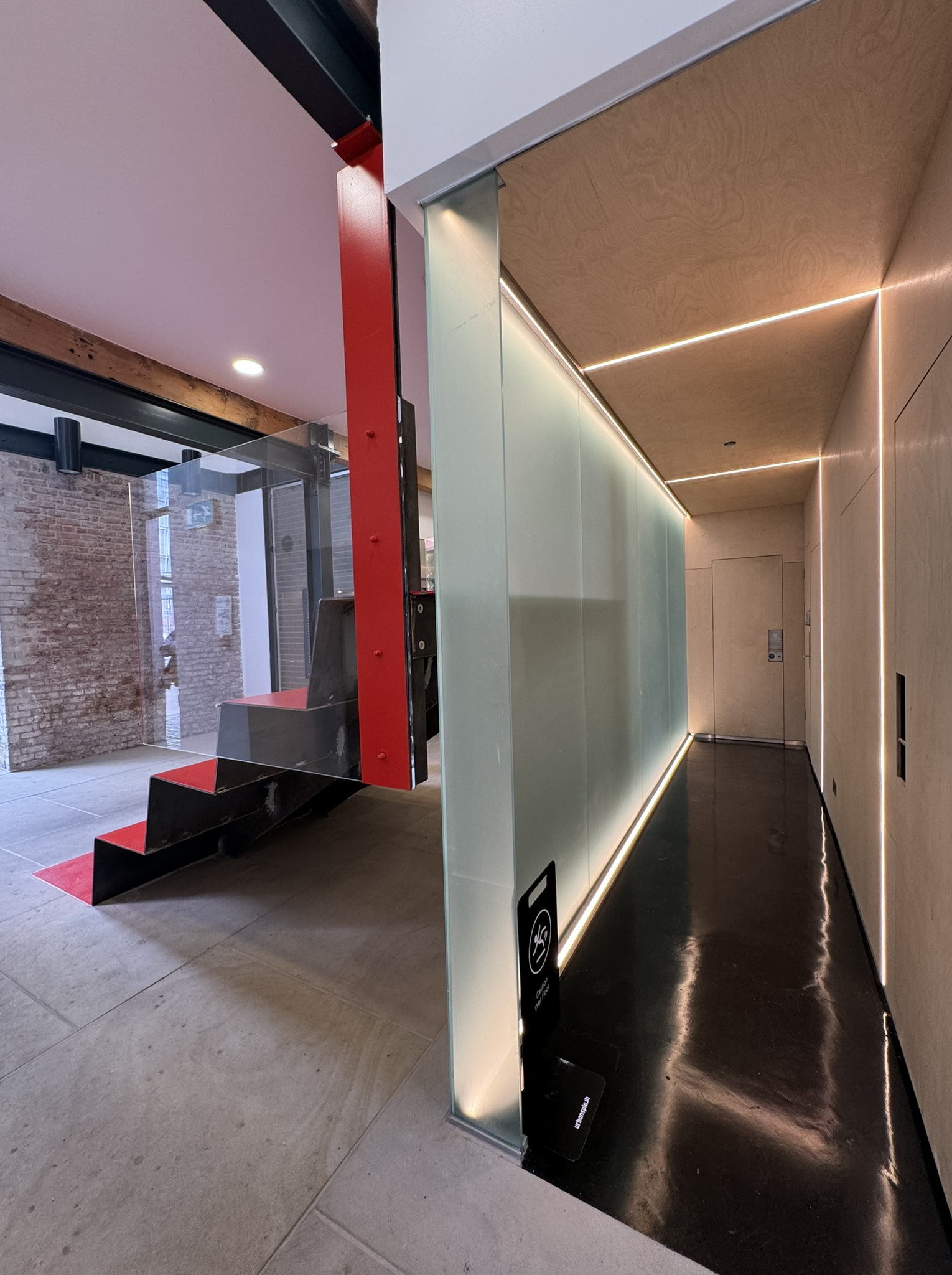 Reception area — red column, glowing glass screen, birch ply corridor
